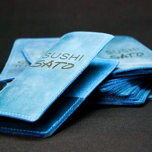 May include: A stack of blue leather menu covers with the text "SUSHI SATO" embossed on the front.
