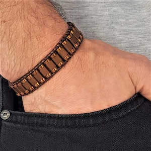 Peut inclure: Un bracelet en cuir marron avec des maillons métalliques de couleur cuivre. Le bracelet est réglable et présente un design simple et moderne.
