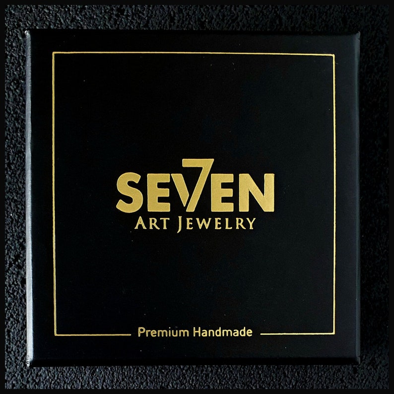 K&ouml;nnte beinhalten: Schwarze Box mit goldener Umrandung und dem Text "SEVEN ART JEWELRY" in goldenen Buchstaben. Der Text "Premium Handmade" ist ebenfalls in goldenen Buchstaben am unteren Rand der Box.