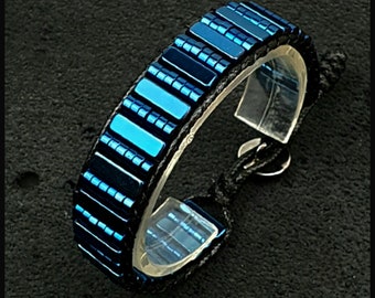 Può includere: Un braccialetto blu fatto di piccole piastrelle rettangolari, con chiusura a cordoncino nero.