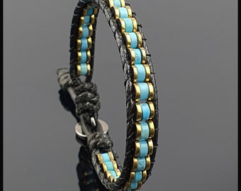 Può includere: Bracciale avvolgente in pelle nera con perline turchesi e dorate. Il bracciale presenta un design intrecciato con chiusura a bottone. Le perline turchesi sono uniformemente distanziate tra le perline dorate.