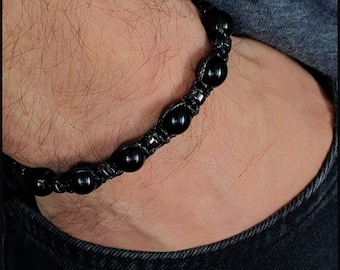 May include: A black beaded bracelet with a braided cord. The beads are round and have a matte finish.