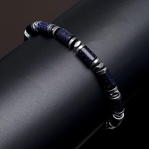 May include: A blue and silver beaded bracelet with a textured, speckled finish. The bracelet is made of small, cylindrical beads with silver accents.