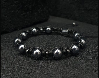 May include: A black beaded bracelet with a magnetic clasp. The beads are round and have a shiny, metallic finish. The bracelet is made with black cord.