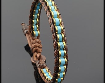 Può includere: Un braccialetto in pelle marrone con perline turchesi e dorate. Il braccialetto è intrecciato con un cinturino in pelle intrecciato.