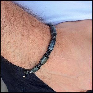 May include: A black bracelet with dark grey beads and black string. The bracelet is made of natural stone and is a stylish accessory for men.