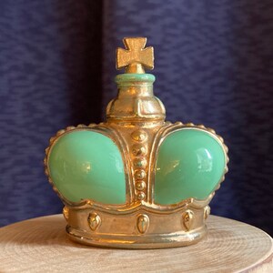 May include: A decorative crown-shaped object with a gold-coloured frame and a light green centre. The crown has a cross on top and is sitting on a wooden surface. The background is a dark blue fabric.