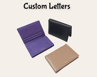 May include: Three leather card holders with custom initials. The card holders are in purple, black, and beige.
