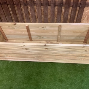 May include: A large, rectangular wooden planter box with a slatted design. The planter is made of natural wood and has a rustic look.