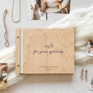 May include: A rectangular light-coloured wooden photo album with a spiral binding featuring two gold-toned metal fasteners. The cover is engraved with a floral sprig, the text "for your eyes only," and the inscription "Love you forever and always Kristen."