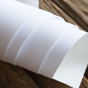 Puede incluir: Un rollo de tela de lienzo blanco, enrollado firmemente y parcialmente desenrollado, revelando la superficie texturizada. El lienzo est&aacute; sobre una superficie de madera.