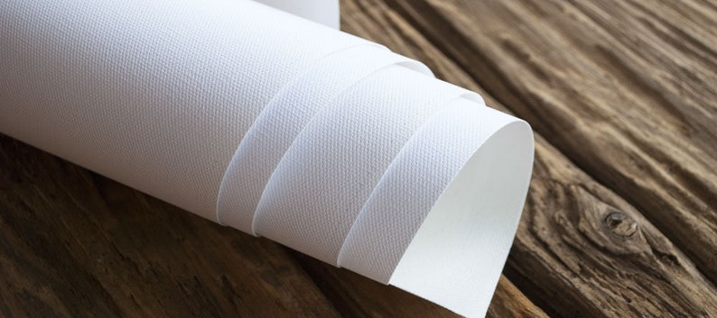 Puede incluir: Un rollo de tela de lienzo blanco, enrollado firmemente y parcialmente desenrollado, revelando la superficie texturizada. El lienzo est&aacute; sobre una superficie de madera.