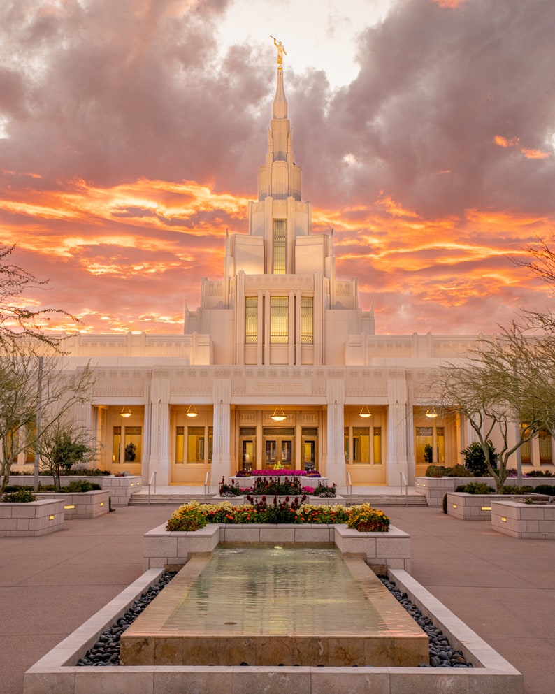 Puede incluir: Un templo blanco con una alta aguja y una estatua en la cima. El templo est&aacute; rodeado de un patio con una fuente y flores. El cielo es de un naranja y rosa vibrantes.