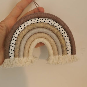 May include: A brown and white polka dot fabric rainbow wall hanging with beige and cream yarn strands. The rainbow has a fringe at the bottom.