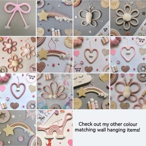 Pode incluir: Uma cole&ccedil;&atilde;o de decora&ccedil;&otilde;es de parede artesanais em v&aacute;rias formas, incluindo la&ccedil;os, estrelas, borboletas, flores e cora&ccedil;&otilde;es. A paleta de cores &eacute; principalmente rosa, creme e dourado, com alguns itens com detalhes de arco-&iacute;ris. O texto diz: "Check out my other colour matching wall hanging items!"