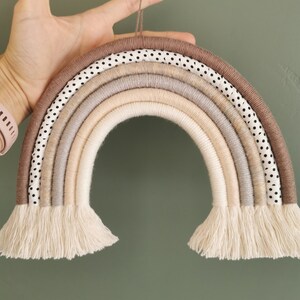 May include: A brown and beige rainbow wall hanging made of yarn and fabric with white polka dots. The rainbow has a fringe at the bottom.