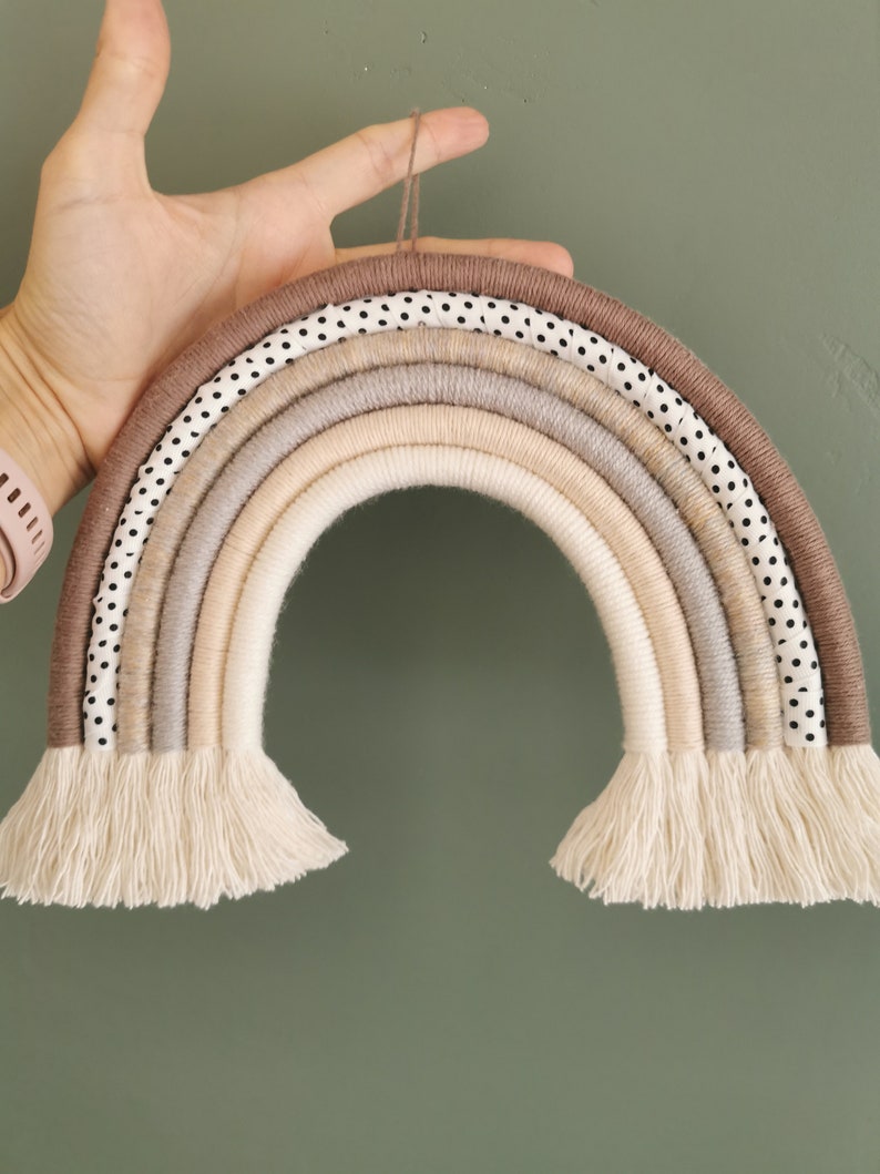 May include: A brown and beige rainbow wall hanging made of yarn and fabric with white polka dots. The rainbow has a fringe at the bottom.