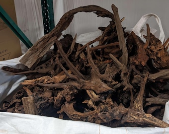May include: A large white bag filled with various pieces of driftwood. The wood pieces are primarily brown with a range of textures and shapes, including branches and root structures. The bag is open, revealing the contents.