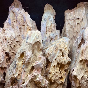 May include: A collection of beige and tan textured rocks with holes and crevices. The rocks have a rough, weathered appearance, suggesting they are natural formations. The image is well-lit, highlighting the details of the rock surfaces.