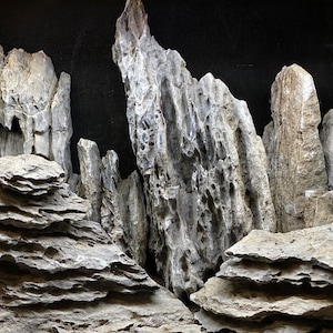 May include: A close-up of a rock formation with tall, jagged peaks and layered, flat rocks. The rocks are a light gray color with some brown and black accents.