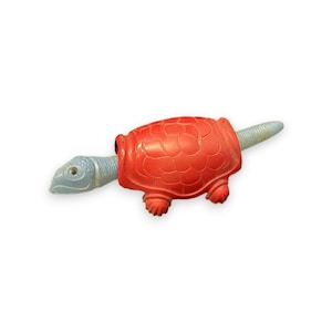 May include: A red plastic toy turtle with a blue head and tail. The turtle has a textured shell and is in a walking position.