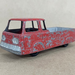 May include: A vintage red toy truck with a silver grill and bed. The truck shows signs of wear, with paint chipping off the metal body. The toy has black wheels and a simple design, evoking a sense of nostalgia.