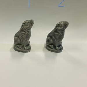 Könnte beinhalten: Zwei kleine graue Keramikfiguren eines sitzenden Hundes, der nach oben schaut. Die Figuren sind identisch und befinden sich auf einem weißen Hintergrund.