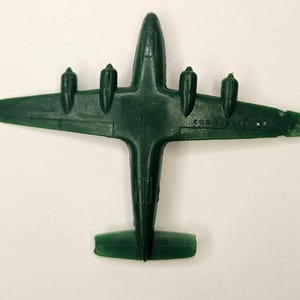 May include: A dark green plastic toy aeroplane with four engines. The aeroplane has a simple design with no markings or details.