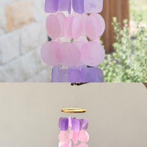 May include: A capiz shell wind chime in shades of purple and pink. The chime features square and round capiz shells suspended from a wooden top. The text on the image reads "THE BEST COLOR SELECTION purple pink capiz shell wind chime."
