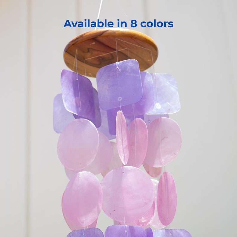 May include: A hanging wind chime with a wooden top and strands of purple and pink shell-shaped pieces. The text "Available in 8 colors" is displayed in blue. The chime is designed for outdoor or indoor decor.