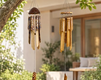May include: Two hanging wind chimes made of natural bamboo tubes. The left chime features a dark coconut shell top and etched floral patterns on the bamboo. The right chime has a circular wooden frame. Both hang from thin black strings.