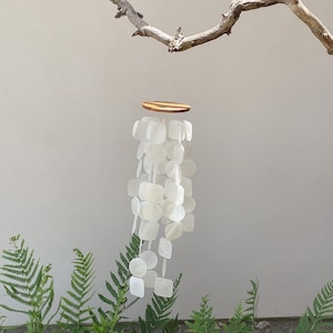 May include: A hanging mobile featuring a circular wooden top piece with a natural grain pattern, from which multiple strands of translucent, square and circular white capiz shell discs are suspended, creating a layered, cascading effect.