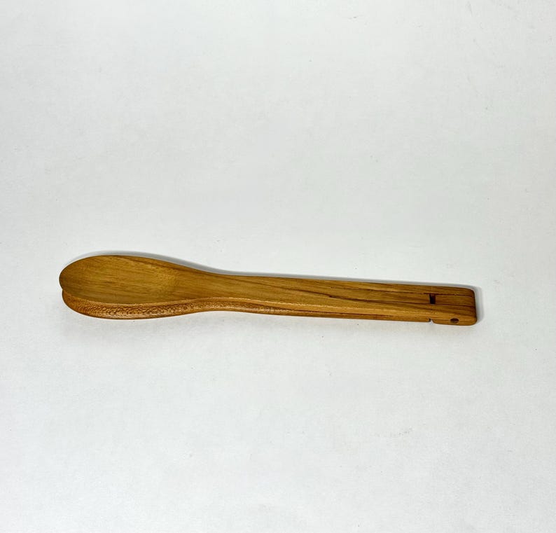 May include: A wooden spoon with a rounded bowl and a rectangular handle. The spoon is made of light brown wood and has a small hole at the end of the handle. The spoon is designed for cooking and serving.