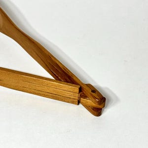 May include: A wooden clothes hanger with a natural finish. The hanger has a rectangular bar and a curved top with a hook. The wood grain is visible, and the hanger appears to be new.