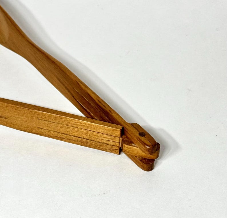 May include: A wooden clothes hanger with a natural finish. The hanger has a rectangular bar and a curved top with a hook. The wood grain is visible, and the hanger appears to be new.