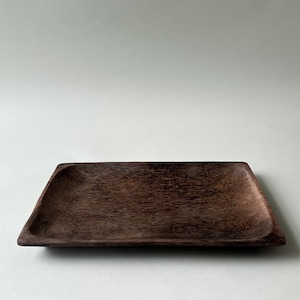 May include: A rectangular wooden tray with a dark brown finish and a visible natural wood grain texture. The tray features slightly raised edges and a shallow, flat center, showcasing a simple, functional design with a smooth, matte appearance.