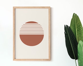 May include: A framed art print featuring a minimalist design of a sun. The artwork is divided into two sections: a lower solid terracotta circle and an upper section of horizontal lines. The frame is made of light-colored wood.