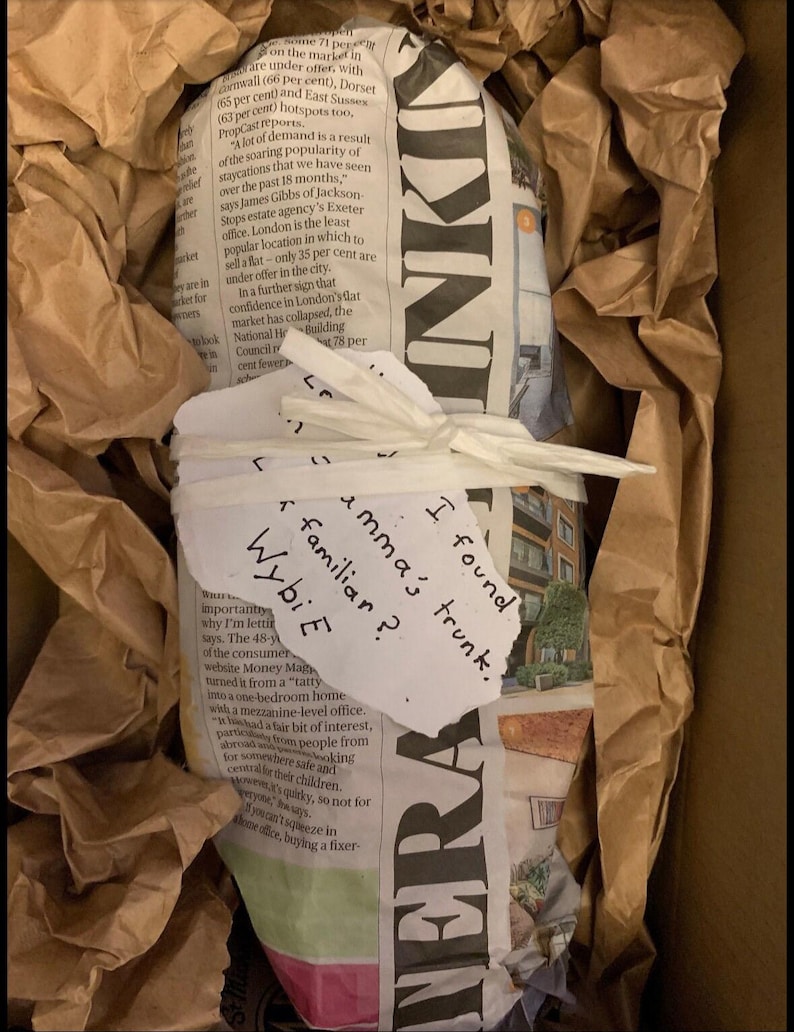 May include: A package wrapped in newspaper and brown paper, inside a cardboard box. A handwritten note on the package reads "I found emma's trunk. Wybi E familiar?"