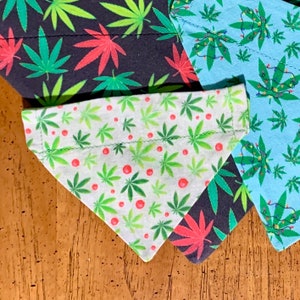May include: A collection of dog bandanas with cannabis leaf patterns. One bandana is white with green leaves and red dots. Other bandanas are dark blue and light blue with green and red leaves, and some with Christmas lights.