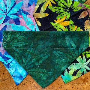 May include: A green bandana with a leaf pattern is centered in the image, surrounded by fabric pieces with similar leaf designs in various colors. The fabrics are pinned to a wooden surface, showcasing a handmade craft project.