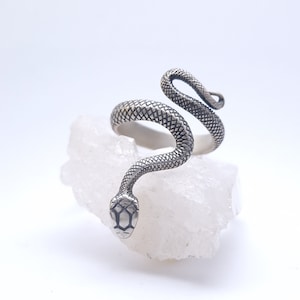 May include: A silver snake ring with a detailed, textured design. The snake is coiled and the head is facing forward.
