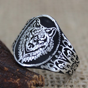 Könnte beinhalten: Ein silberner Ring mit einem Wolfskopf-Design. Der Ring ist oval geformt und hat komplizierte Details um den Wolfskopf herum.