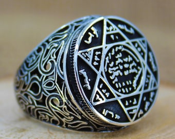 May include: A silver ring with a black, engraved design featuring a six-pointed star and Arabic script.