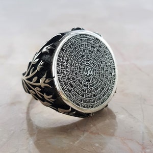 Puede incluir: Un anillo de plata con un dise&ntilde;o circular que presenta escritura &aacute;rabe y la palabra "Allah" en el centro. El anillo tiene un dise&ntilde;o floral en la banda.