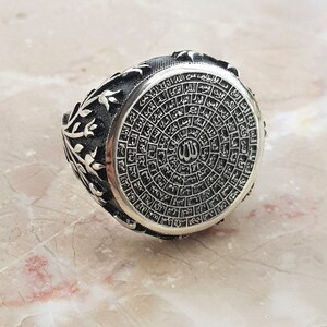 Puede incluir: Un anillo de plata con un dise&ntilde;o intrincado que presenta escritura &aacute;rabe y la palabra "Allah" en el centro. El anillo tiene un patr&oacute;n floral en los lados.