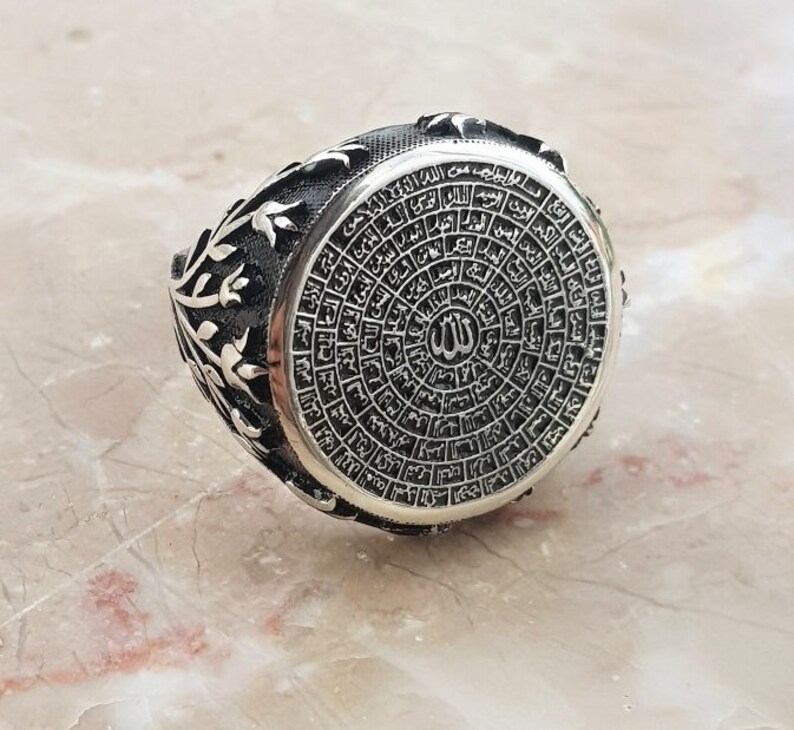 Puede incluir: Un anillo de plata con un dise&ntilde;o intrincado que presenta escritura &aacute;rabe y la palabra "Allah" en el centro. El anillo tiene un patr&oacute;n floral en los lados.