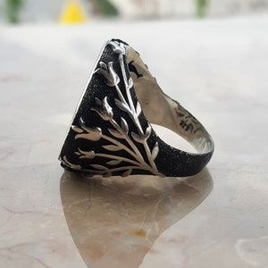 Puede incluir: Un anillo de plata con una piedra negra y un dise&ntilde;o floral. El anillo est&aacute; hecho de plata de ley y tiene un acabado texturizado.