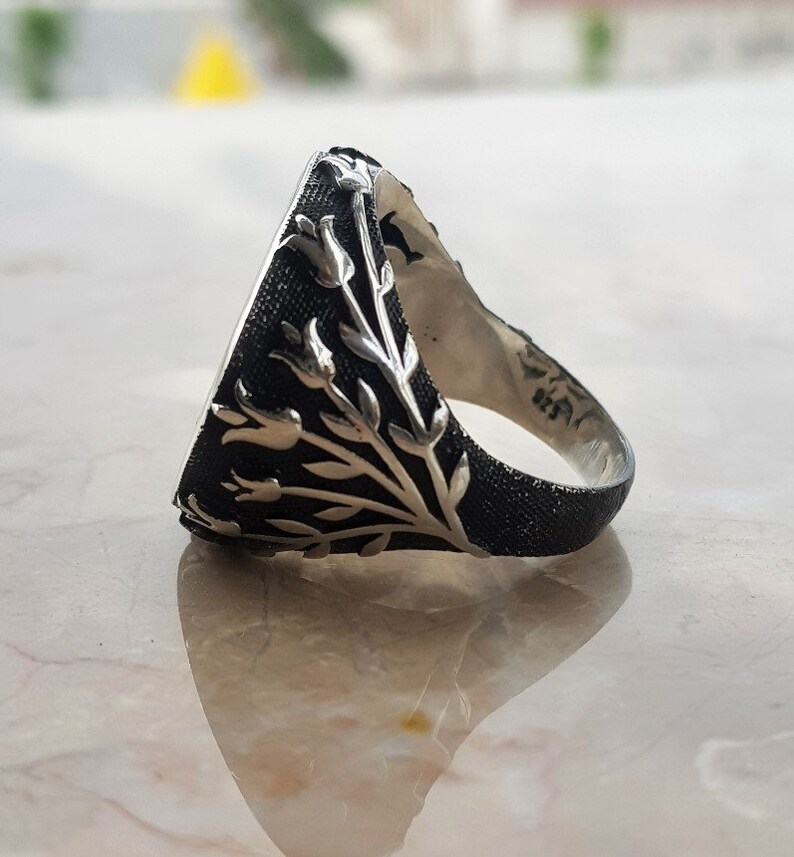 Puede incluir: Un anillo de plata con una piedra negra y un dise&ntilde;o floral. El anillo est&aacute; hecho de plata de ley y tiene un acabado texturizado.