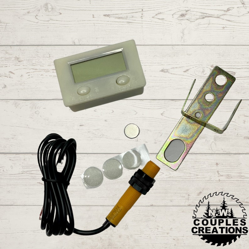 May include: A white digital counter with two buttons, a yellow sensor with a black wire, a metal bracket, four white adhesive pads, and a small silver disc. The counter has a digital display and the sensor has a black wire attached to it. The metal bracket has three holes in it. The adhesive pads are round and have a sticky back. The silver disc is small and round. The image is on a wooden background.