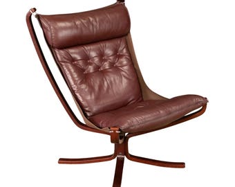 May include: A mid-century modern style chair with a dark brown leather seat and backrest. The chair has a wooden frame and a unique design, with a high back and a comfortable, padded seat. The chair is designed for relaxation and comfort.